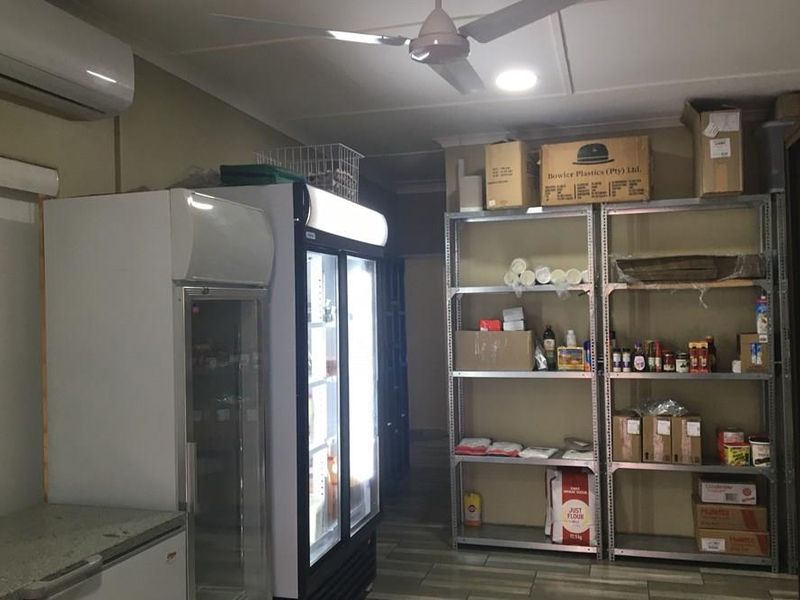 A functional utility or scullery area featuring tiled flooring, ceiling fan, air conditioning, and ample storage shelving for commercial use.
