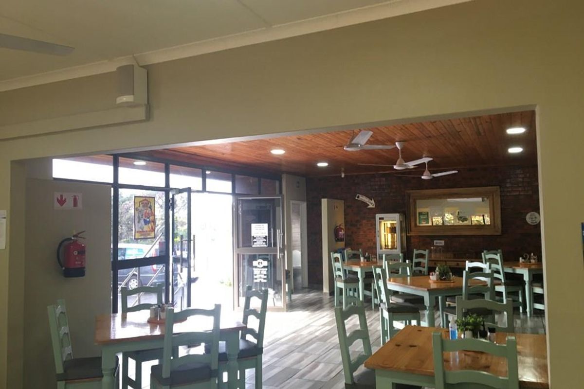 Spacious open-plan commercial dining area featuring a warm timber ceiling, exposed brick accents, tiled flooring, and large glass entrance doors.