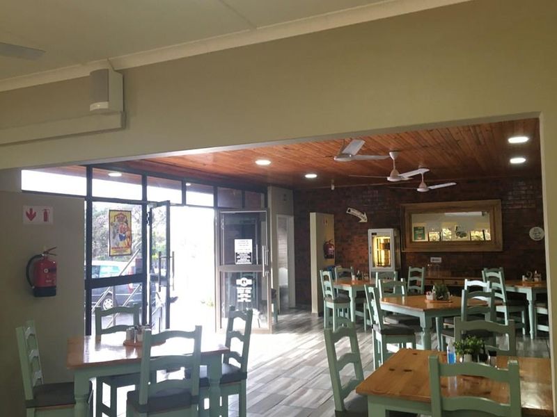 Spacious open-plan commercial dining area featuring a warm timber ceiling, exposed brick accents, tiled flooring, and large glass entrance doors.