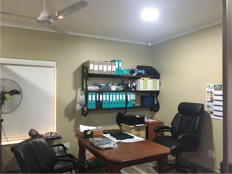 A functional office space featuring a wall-mounted shelving unit, ceiling fan, and roller blind, providing a practical work environment.