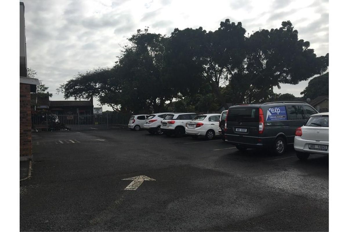A paved commercial parking area featuring metal security fencing and mature trees, providing functional outdoor space for the property.