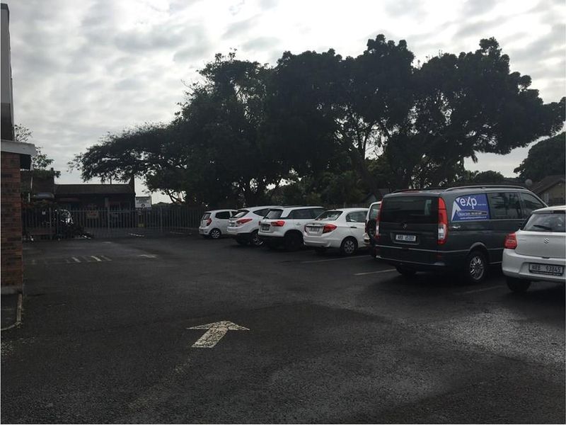 A paved commercial parking area featuring metal security fencing and mature trees, providing functional outdoor space for the property.