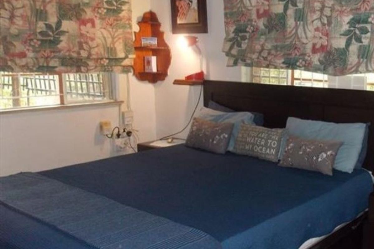 A cozy bedroom featuring a wall-mounted air conditioning unit and dual windows with patterned roman blinds.