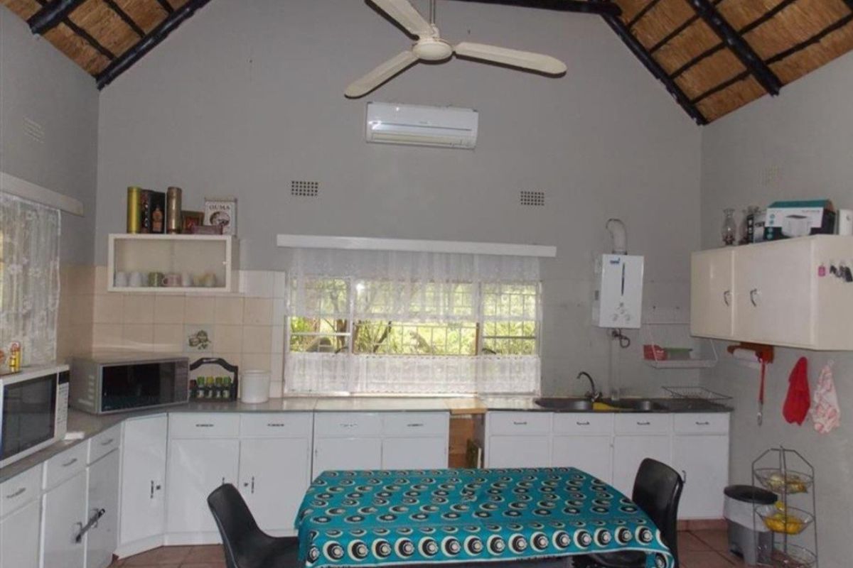 A kitchen featuring a high vaulted thatched ceiling, white cabinetry, tiled flooring, and a wall-mounted air conditioning unit.