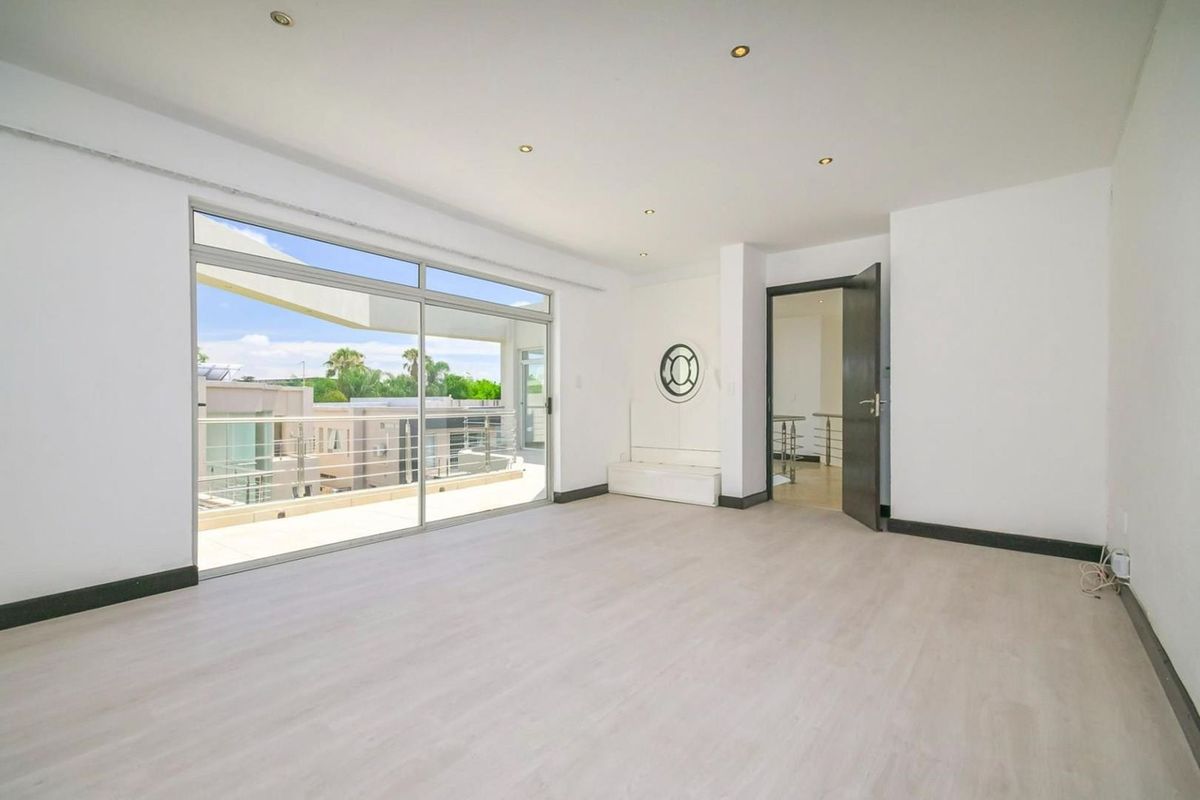 A bright, empty bedroom featuring light-toned laminate flooring, recessed ceiling lighting, and large sliding glass doors opening onto a private balcony.