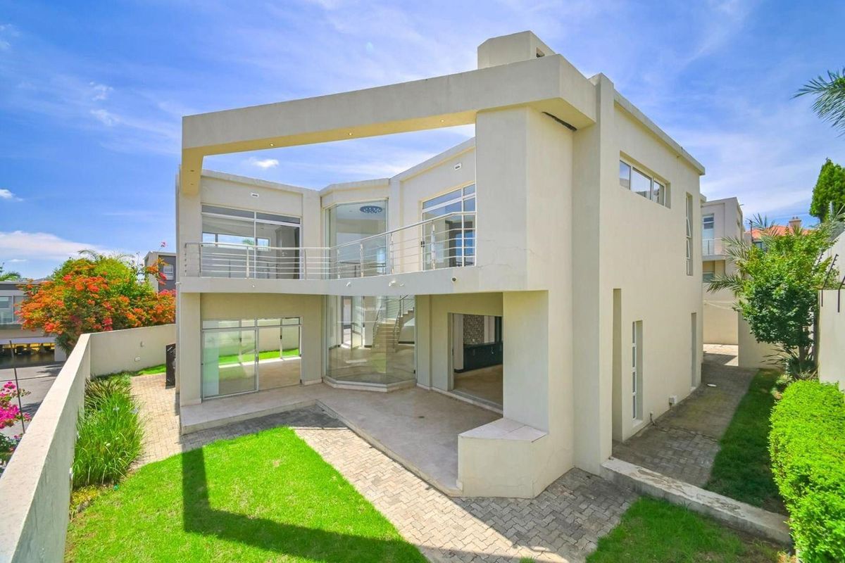 A modern two-story residential property featuring a contemporary architectural design, large glass windows, a balcony, and a paved patio area overlooking the garden.