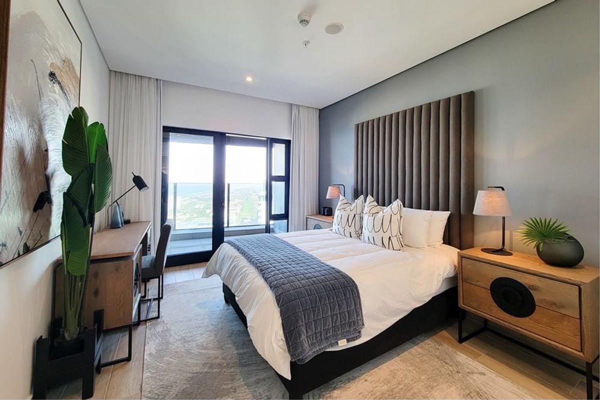 A modern, well-appointed bedroom featuring a floor-to-ceiling headboard, integrated lighting, and sliding glass doors leading to a private balcony with scenic views.