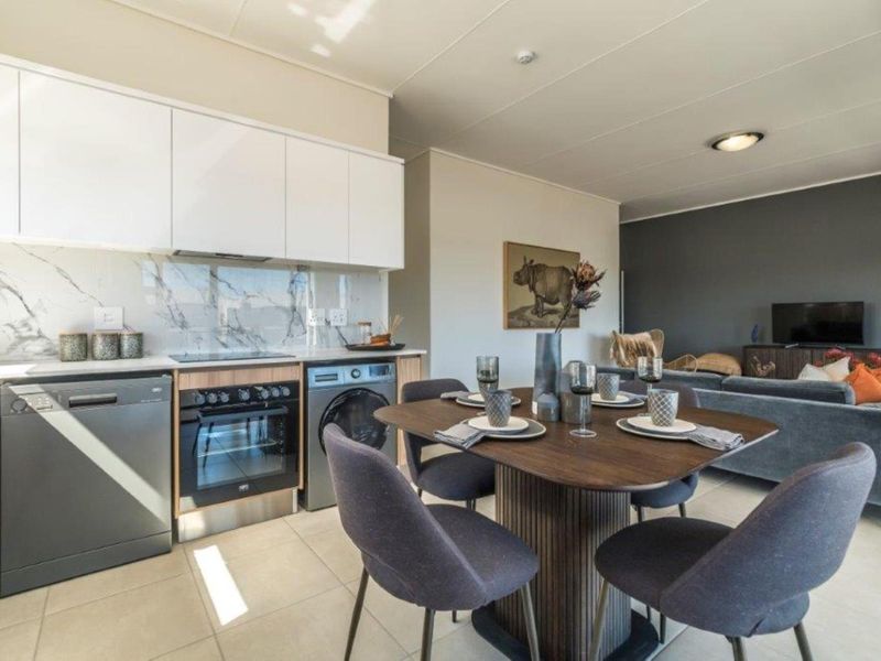 Modern open-plan living area featuring a contemporary kitchen with white cabinetry, marble-look splashback, and integrated appliances, flowing into a dining and lounge space.