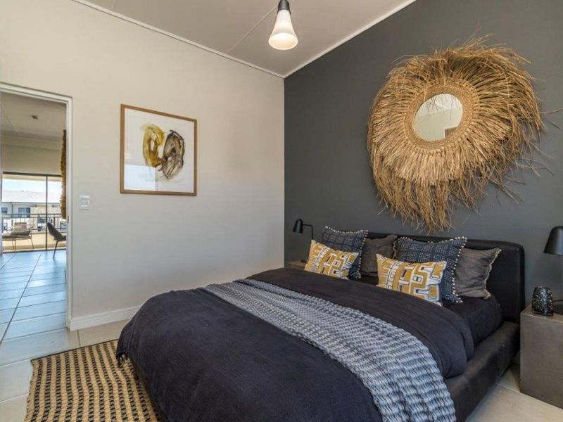 A well-maintained bedroom featuring a dark grey accent wall, neutral tiled flooring, and a doorway leading to an adjacent balcony area.
