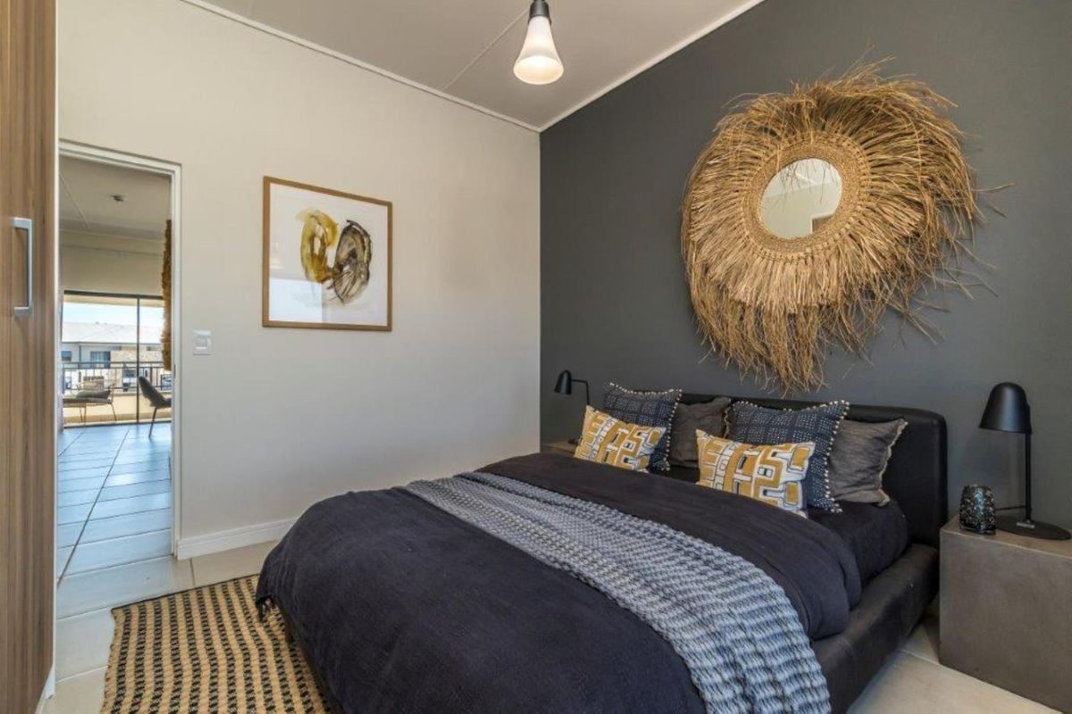 A well-maintained bedroom featuring a dark grey accent wall, neutral tiled flooring, and a doorway leading to an adjacent balcony area.