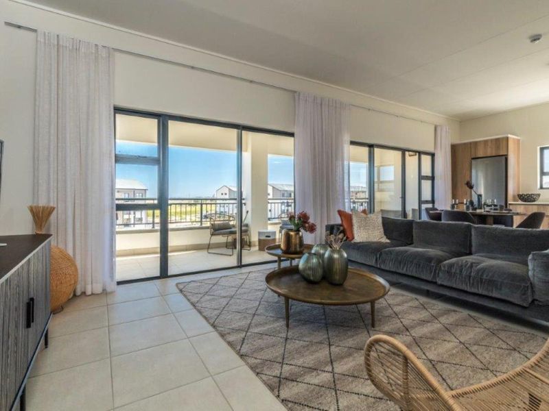 Spacious open-plan living area featuring large sliding glass doors leading to a balcony, tiled flooring, and integrated kitchen cabinetry.