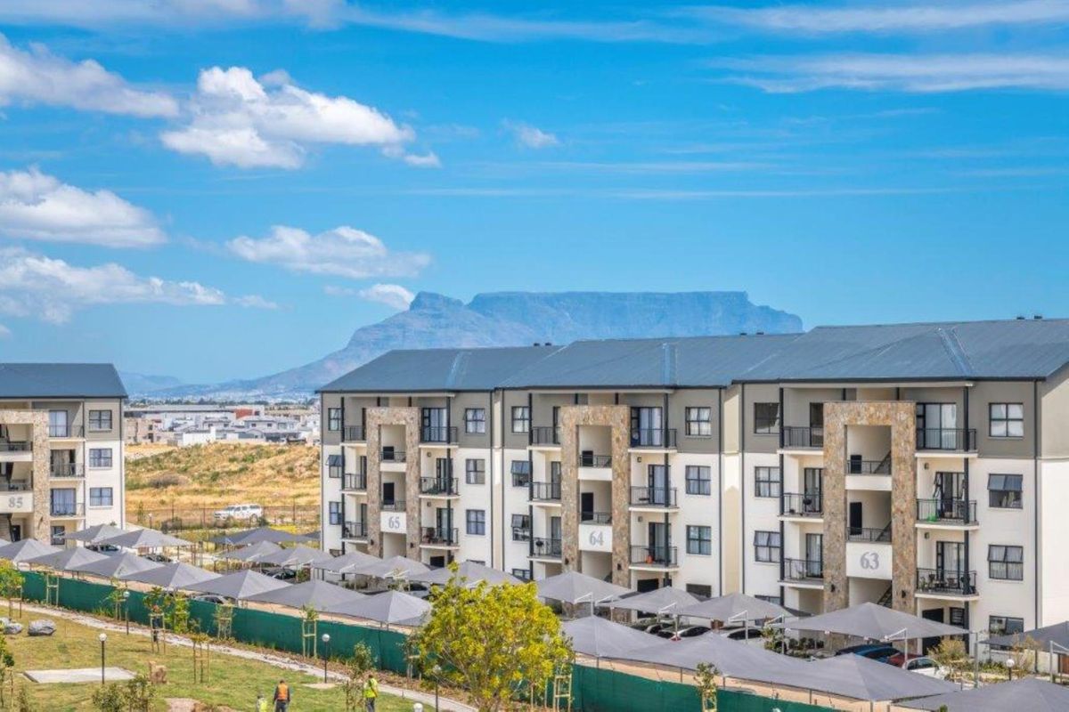 Exterior view of a modern apartment complex featuring stone-clad facades, private balconies, and covered parking bays with a mountain backdrop.