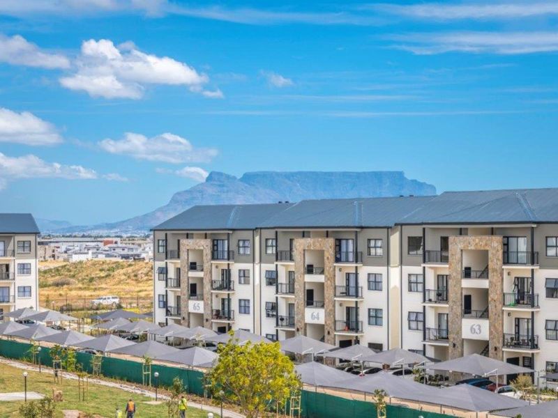 Exterior view of a modern apartment complex featuring stone-clad facades, private balconies, and covered parking bays with a mountain backdrop.