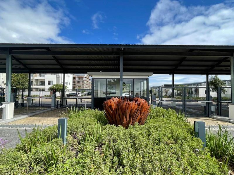 A secure apartment complex entrance featuring a guard house, metal canopy, and automated boom gates for controlled access.