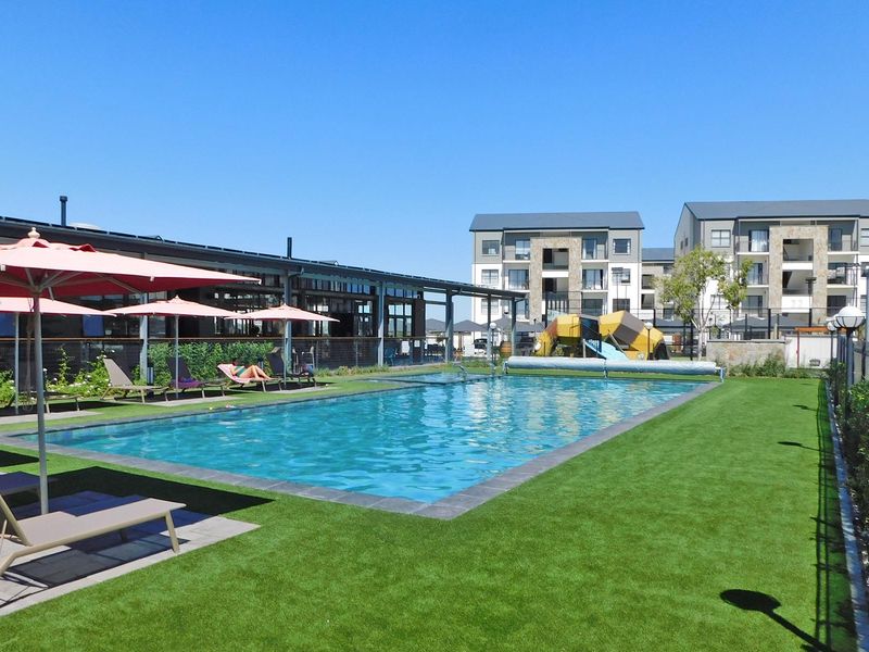Well-maintained communal swimming pool area featuring artificial turf, perimeter fencing, and adjacent outdoor leisure space within an apartment complex.