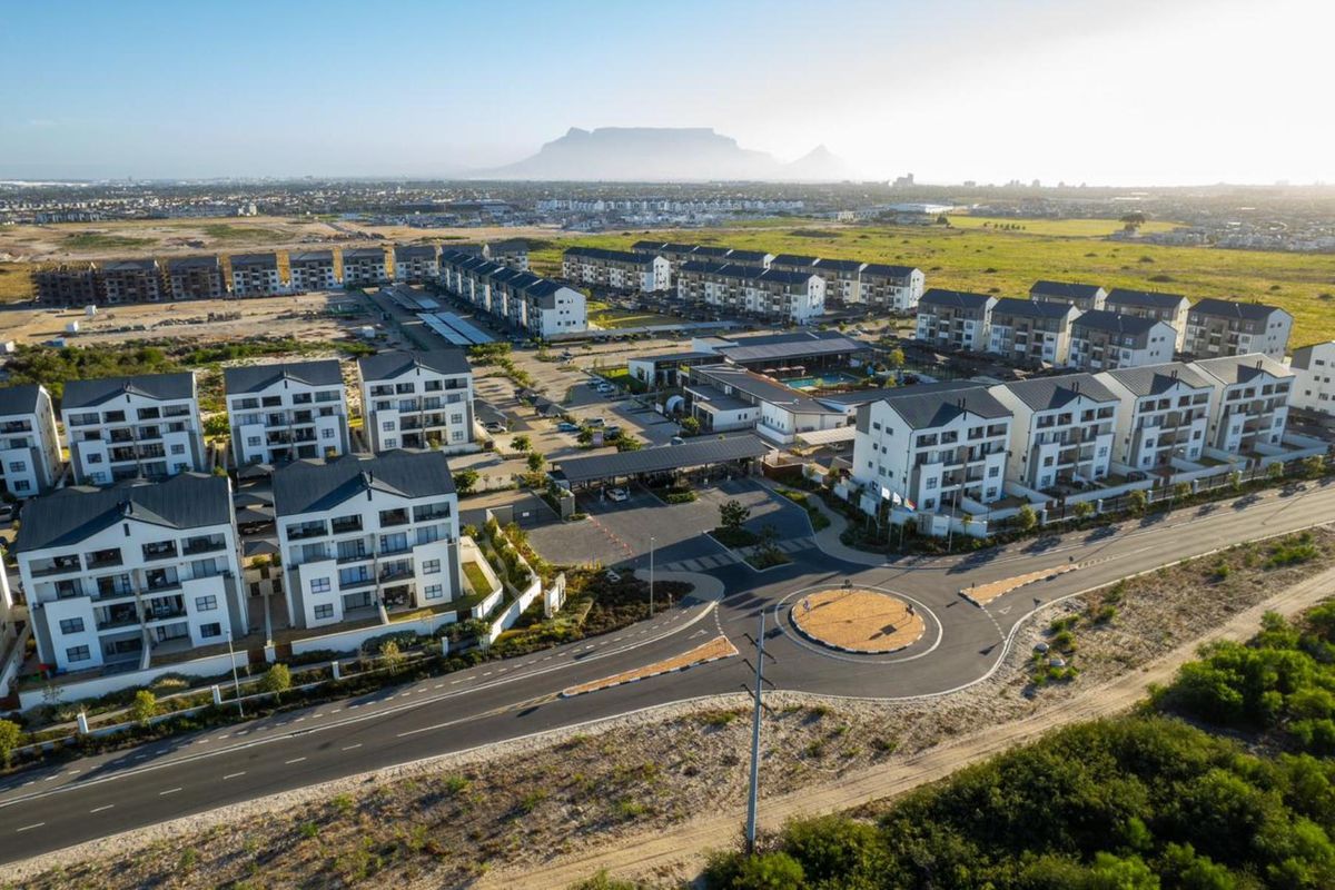 Aerial view of a modern residential apartment complex featuring multiple building blocks, a gated entrance, and communal facilities with Table Mountain in the background.