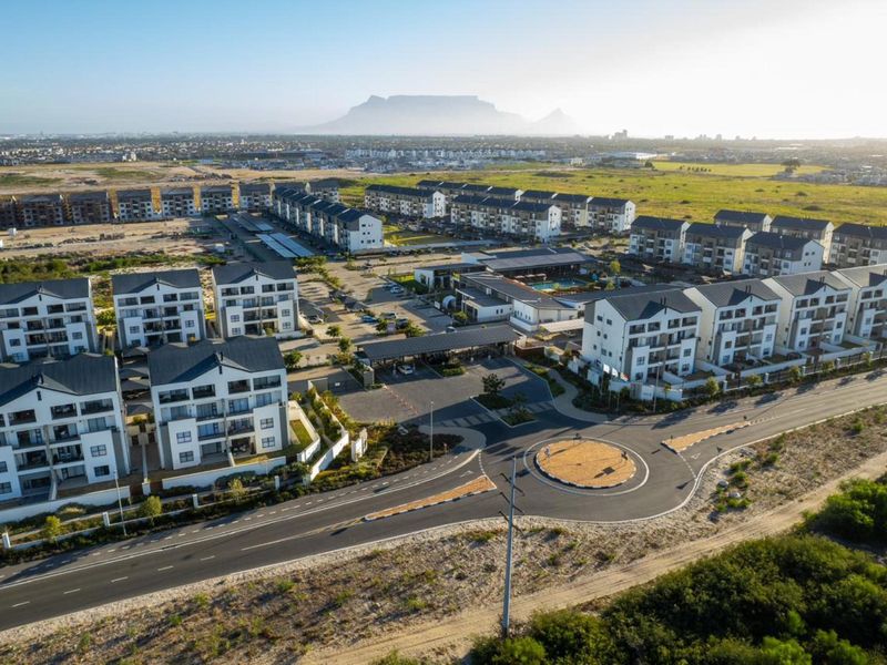 Aerial view of a modern residential apartment complex featuring multiple building blocks, a gated entrance, and communal facilities with Table Mountain in the background.