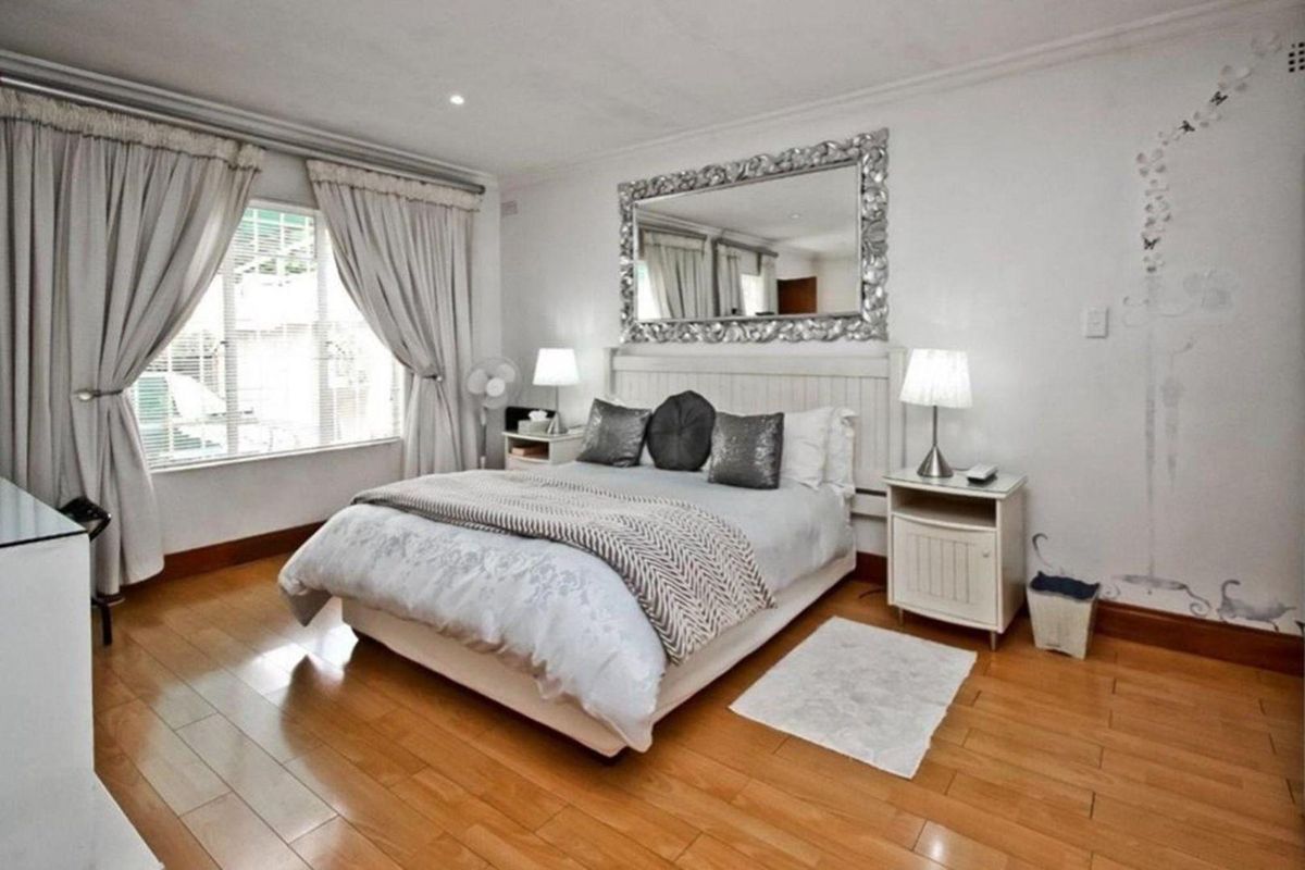A well-lit bedroom featuring polished timber flooring, recessed ceiling lighting, and large windows with curtain tracks.