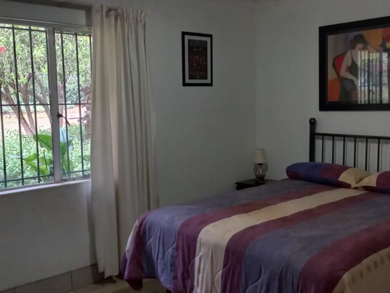 A bedroom featuring tiled flooring and a large window with security bars, offering a view of the garden.