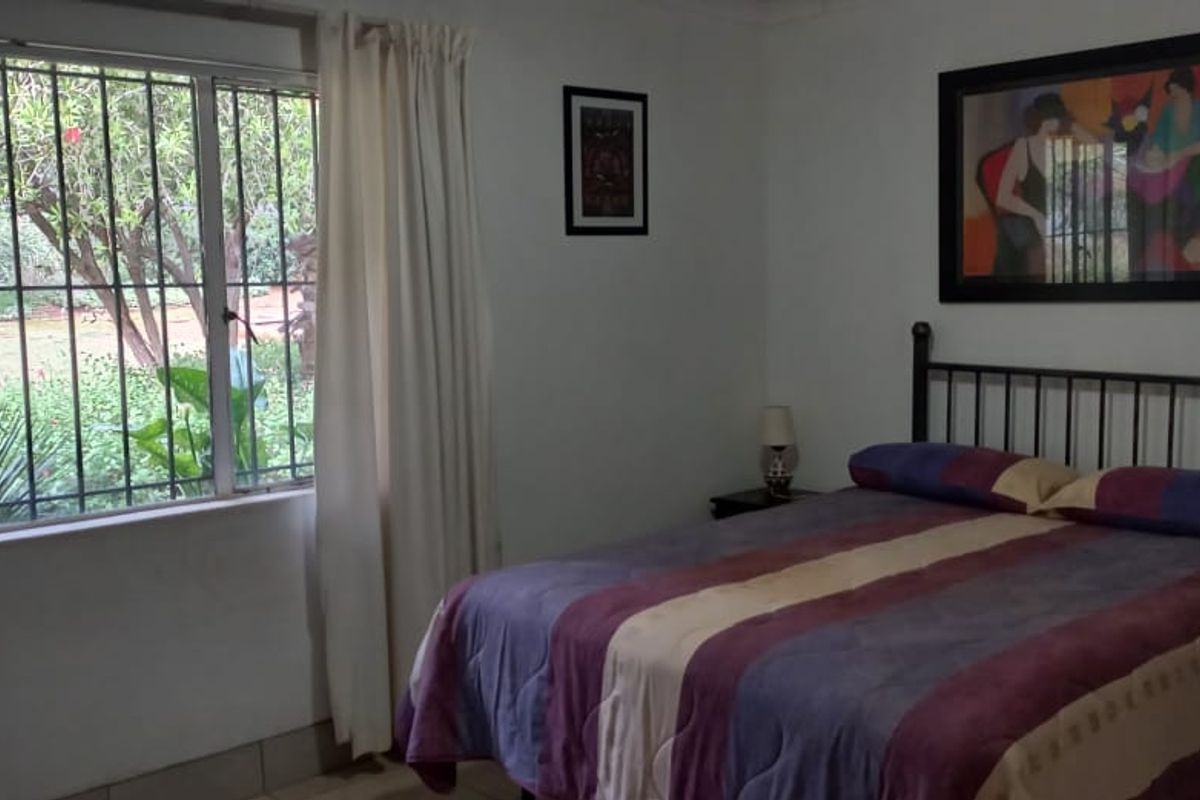 A bedroom featuring tiled flooring and a large window with security bars, offering a view of the garden.