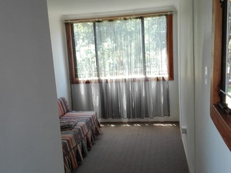 A sunlit living area featuring carpeted flooring, wooden window frames with security bars, and classic cove cornicing.