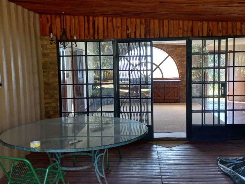 A rustic covered patio area featuring timber decking, wood-paneled ceilings, and large steel-framed glass doors leading to an adjacent living space.