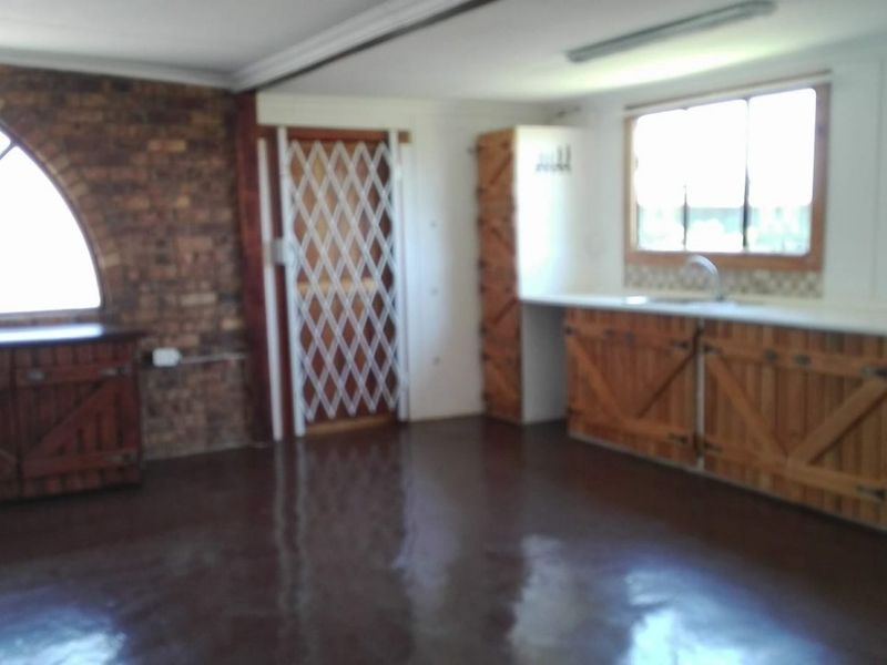 A rustic kitchen area featuring exposed brickwork, an arched window, built-in wooden cabinetry, and polished concrete flooring.