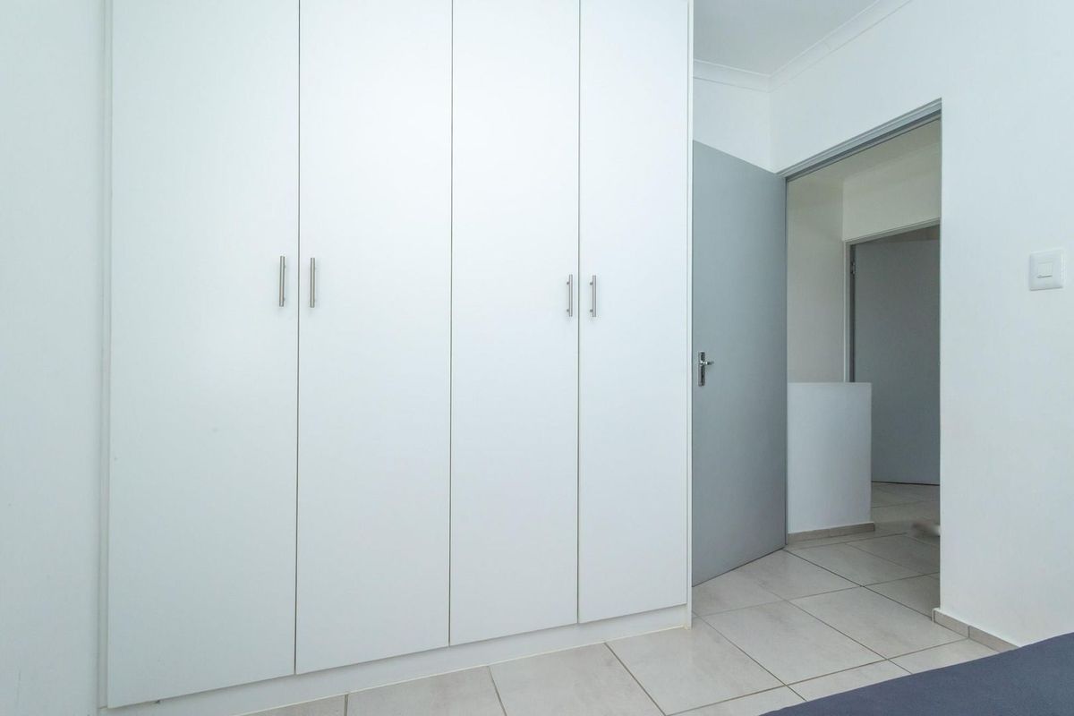 A clean bedroom interior featuring built-in floor-to-ceiling white cabinetry and tiled flooring, leading into an adjacent hallway.