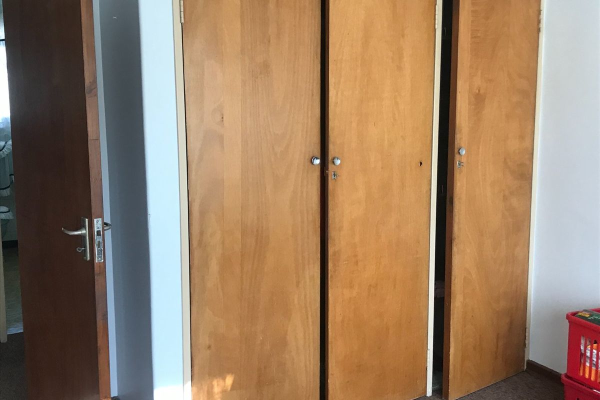 A bedroom interior featuring built-in wooden cupboards with dated finishes and standard door hardware.