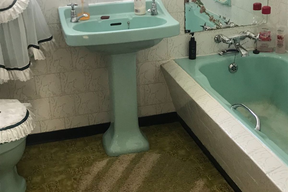 A dated bathroom featuring a vintage mint green pedestal sink and matching bathtub with patterned wall tiles and retro flooring.
