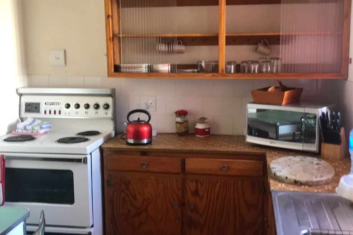 A dated kitchen area featuring wooden cabinetry, a tiled countertop, and a freestanding stove, offering potential for modernization and renovation.