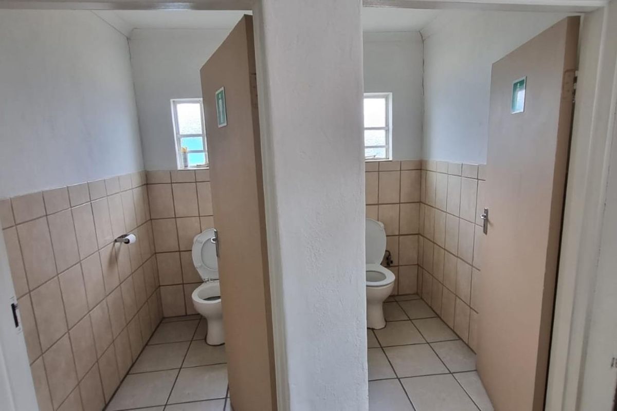 Two separate industrial restroom cubicles featuring tiled walls and floors, each equipped with a standard toilet and privacy door.