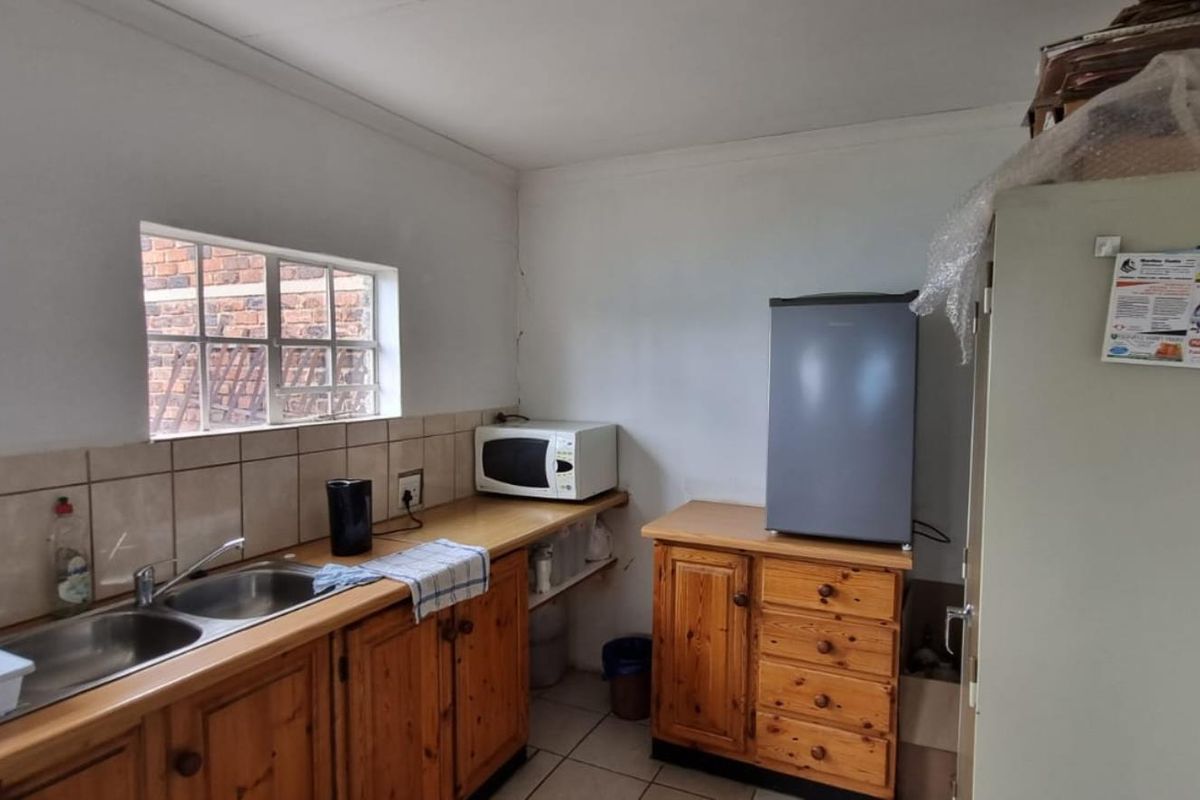 A functional kitchen area featuring wooden cabinetry, a double stainless steel sink, tiled splashbacks, and tiled flooring.