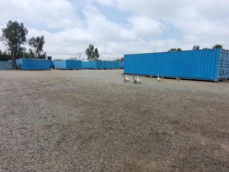 Expansive industrial yard featuring multiple blue shipping containers on a gravel surface, suitable for storage or logistics operations.