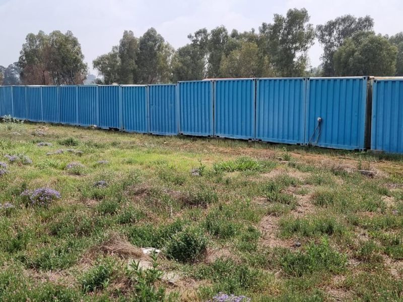 A row of industrial shipping containers positioned on a large, open grassed plot, suitable for storage or site infrastructure.