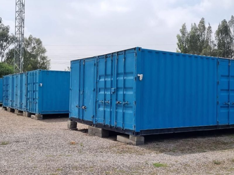 A row of industrial blue shipping containers situated on a gravel yard, suitable for secure storage or modular utility space.