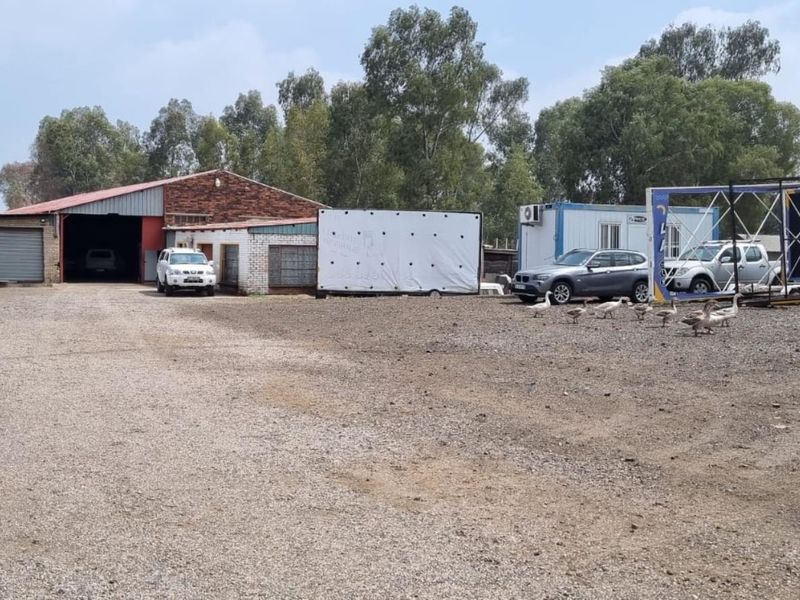 Industrial property featuring a large warehouse structure with roller shutter doors and an expansive gravel yard area.