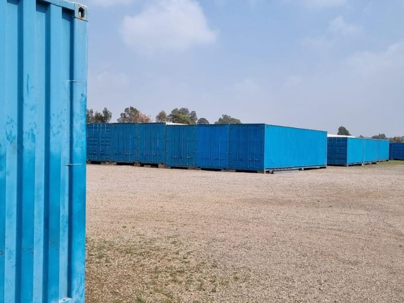 An industrial storage yard featuring multiple blue shipping containers arranged on a gravel lot, suitable for secure storage or logistics operations.