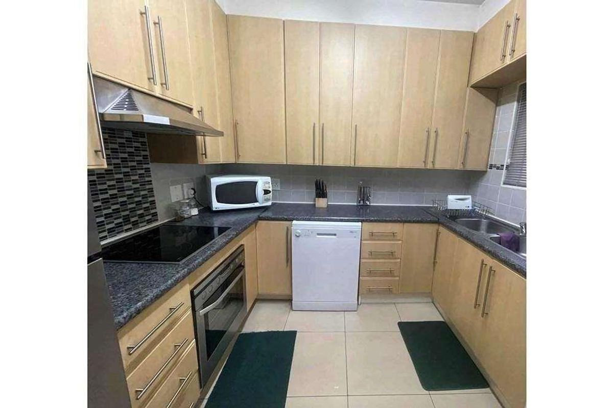 A functional kitchen featuring light wood cabinetry, dark granite countertops, a built-in oven, hob, extractor fan, and a double sink with tiled splashbacks.