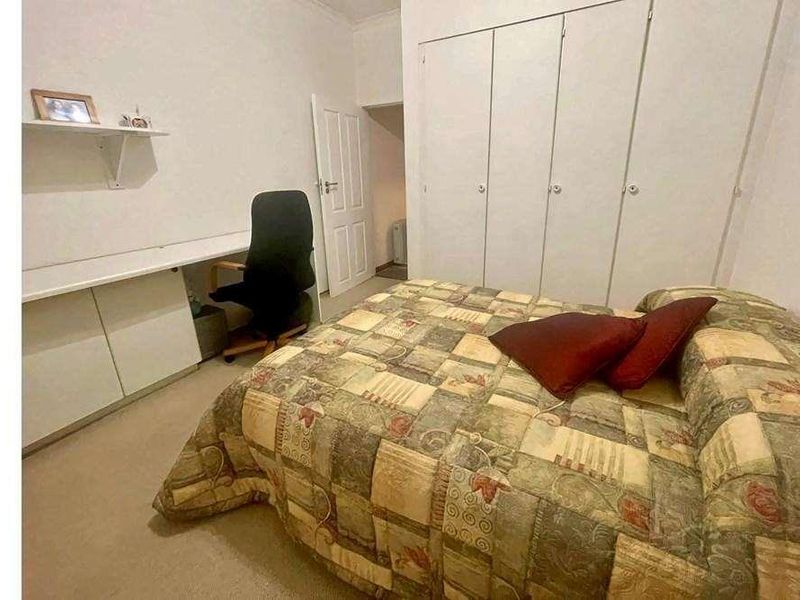 A bedroom featuring built-in wardrobes and a fitted desk area with shelving, providing functional storage and workspace.