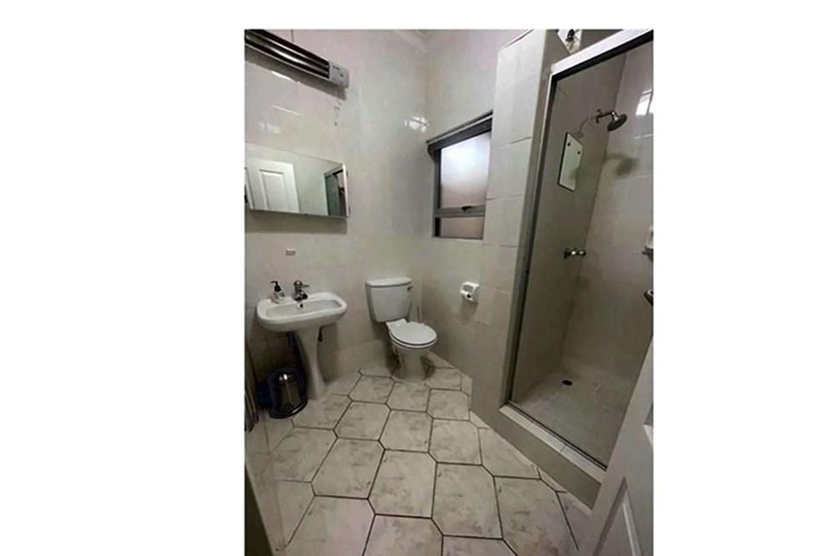 A functional bathroom featuring a pedestal sink, a toilet, and a glass-enclosed shower stall with tiled flooring and wall finishes.