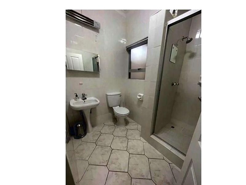 A functional bathroom featuring a pedestal sink, a toilet, and a glass-enclosed shower stall with tiled flooring and wall finishes.