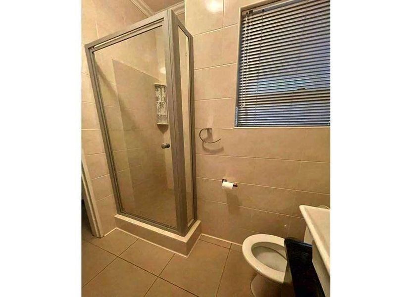 A functional bathroom featuring a glass-enclosed shower, tiled walls and flooring, and a standard toilet.