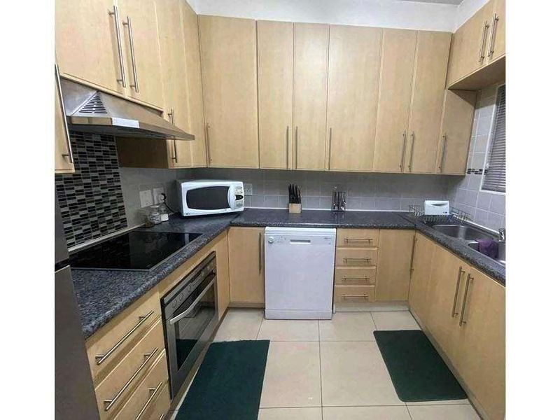 A functional kitchen featuring light wood cabinetry, dark granite countertops, a built-in oven, hob, extractor fan, and a double sink with tiled splashbacks.