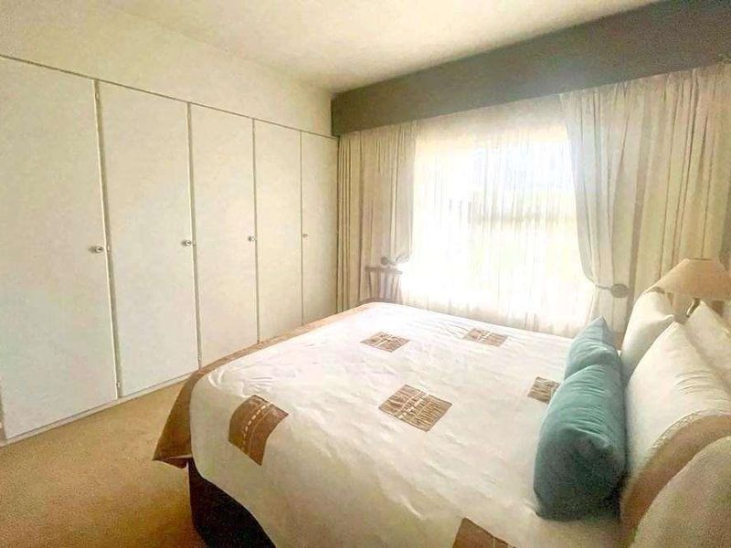 A bedroom featuring wall-to-wall built-in cupboards and a large window with curtain pelmet.