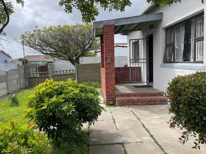 Front entrance featuring a brick porch, security gate, and paved walkway, set within a garden with precast concrete boundary walls.