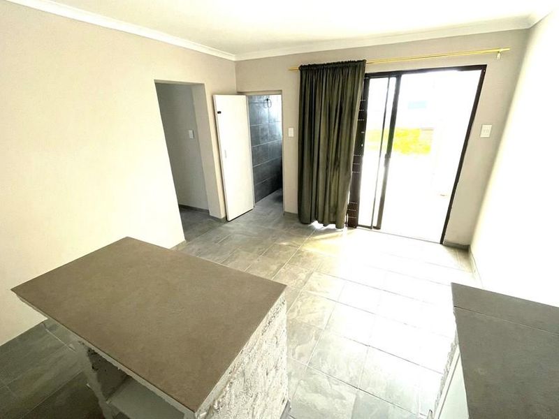 An open-plan living area featuring tiled flooring, a sliding glass door to the exterior, and a central stone-finish island unit.