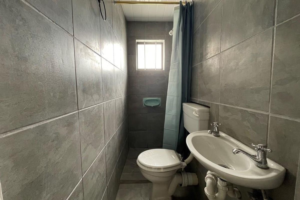 Compact bathroom featuring full-height grey ceramic wall tiling, a pedestal basin, and a toilet, with a small window providing natural light.