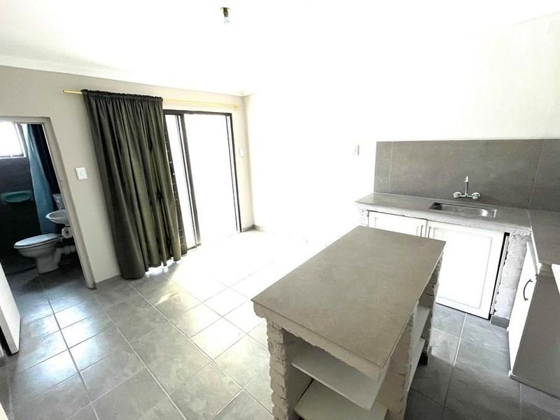 Open plan kitchen and living area featuring tiled floors, a central island, and direct access to an adjoining bathroom through a sliding door.