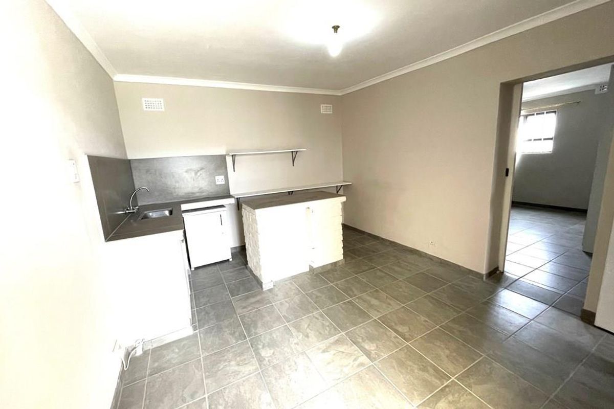 A basic, empty kitchen area featuring tiled flooring, a small sink unit, and built-in shelving, offering a blank canvas for potential renovation.